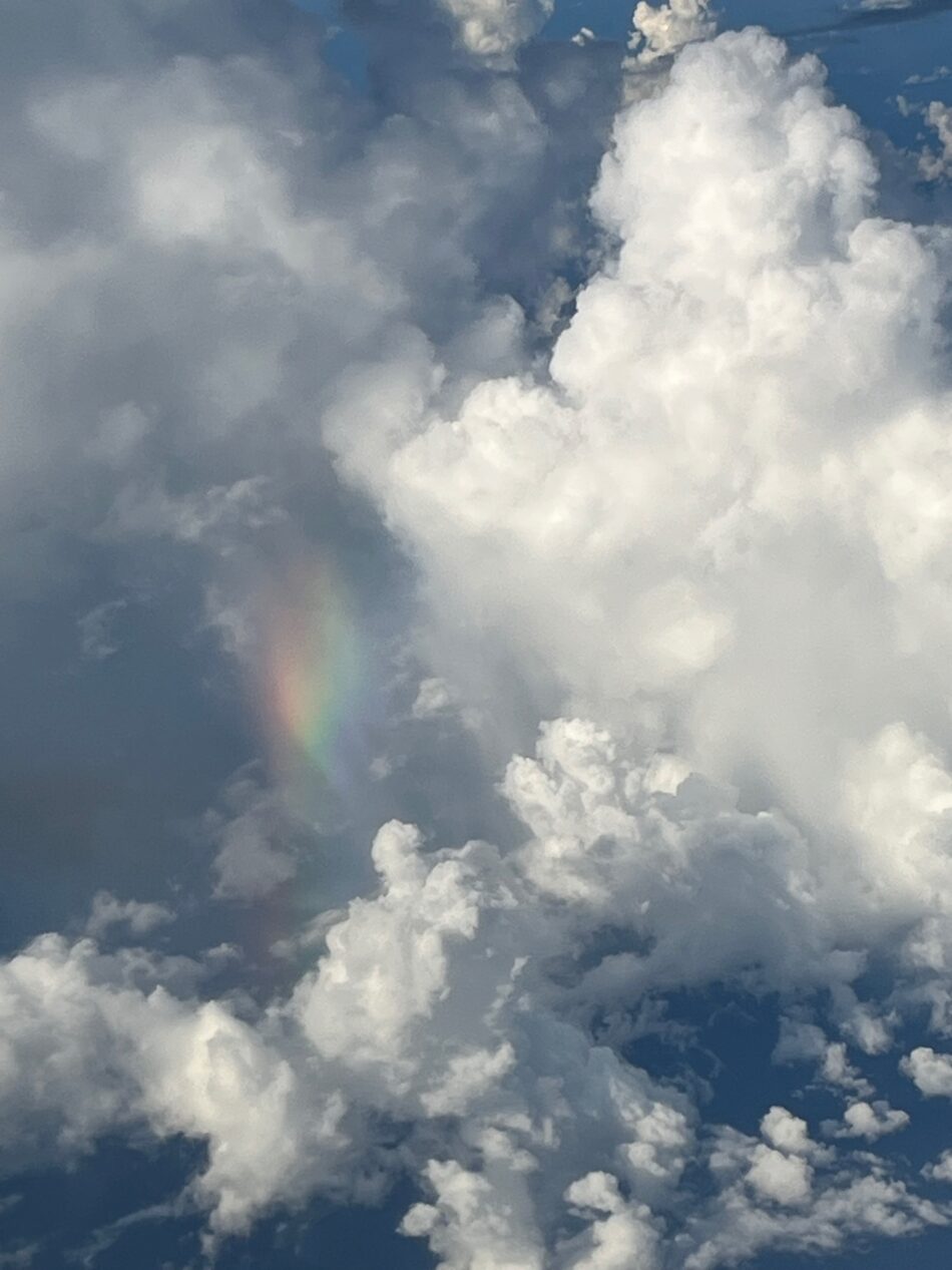 white clouds in the sky with a burst of rainbow, a view from the plane