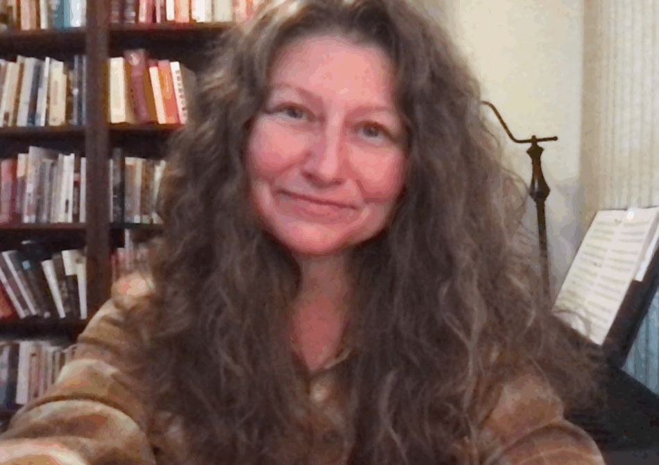 Headshot of me in front of my bookshelves and electronic piano - aka my zoom room